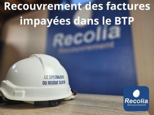 Casque de chantier marqué "Le spécialiste du risque client" devant un panneau Recolia – Recouvrement des factures impayées dans le BTP